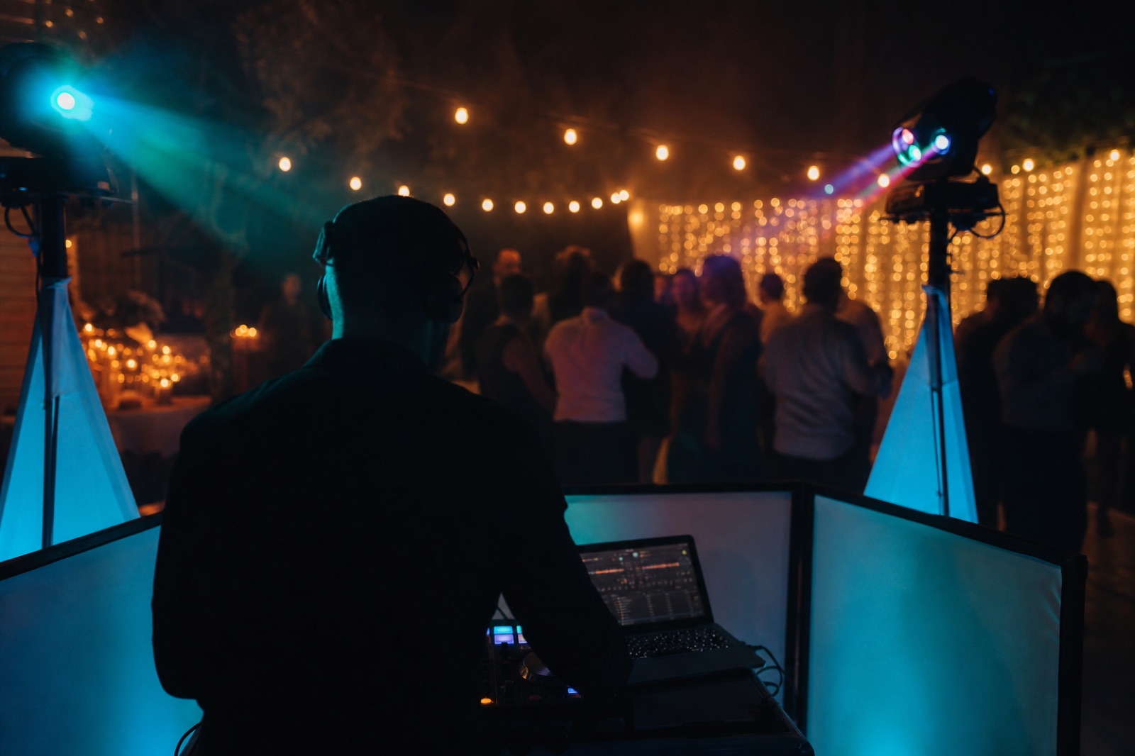 Consolle DJ mobile a una festa privata con luci a filo e un fascio ciano