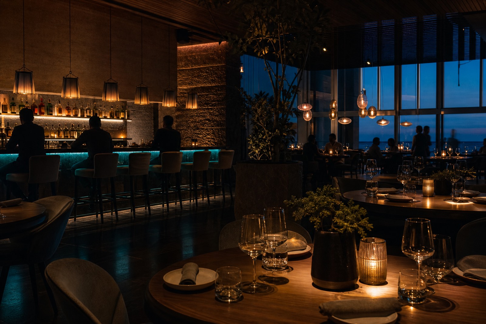 Lounge di un ristorante serale con lampade calde a sospensione e un bancone illuminato in verde acqua